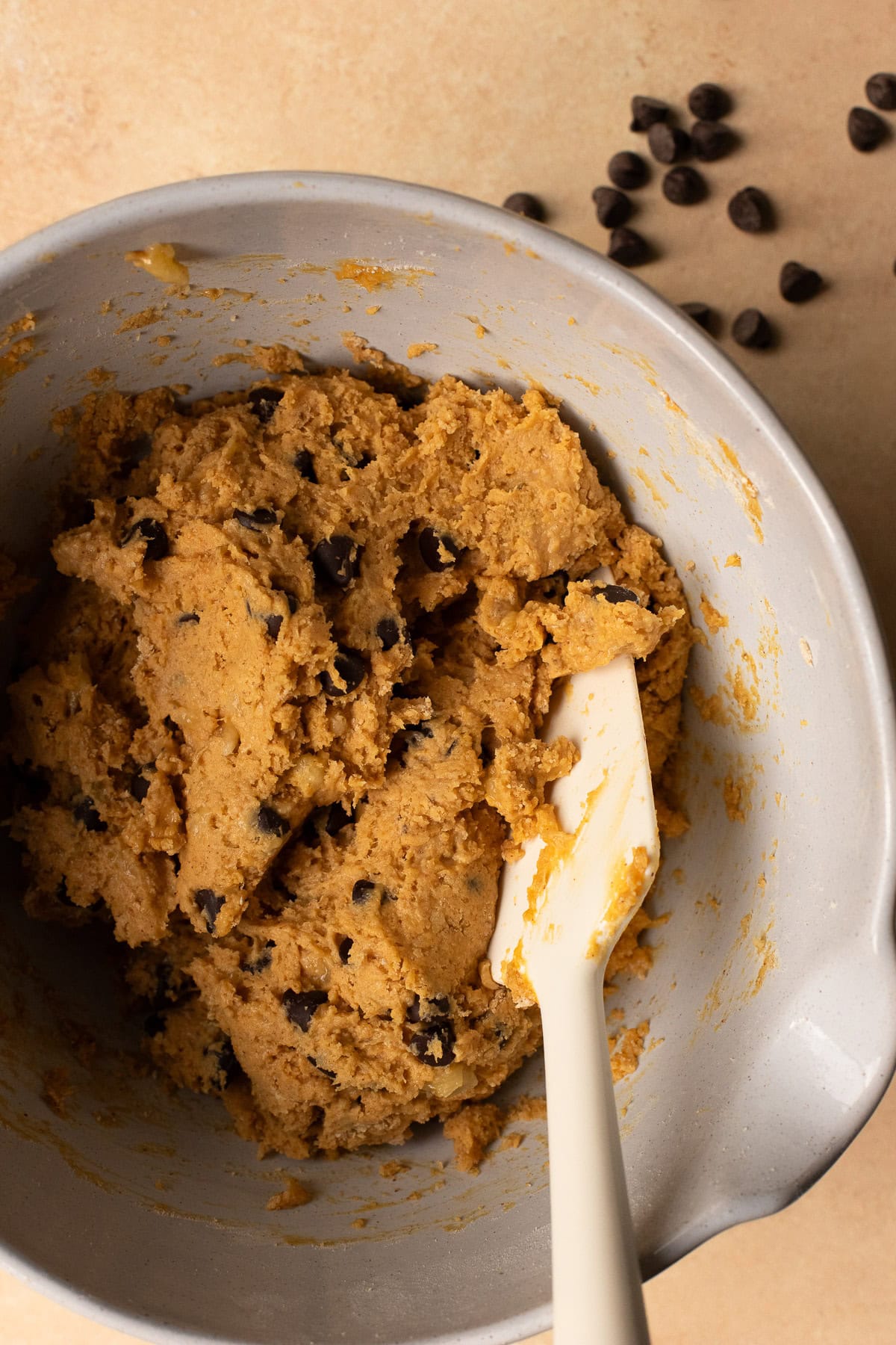 Batter for peanut butter banana protein muffins with chocolate chips mixed together in a bowl with a rubber spatula.