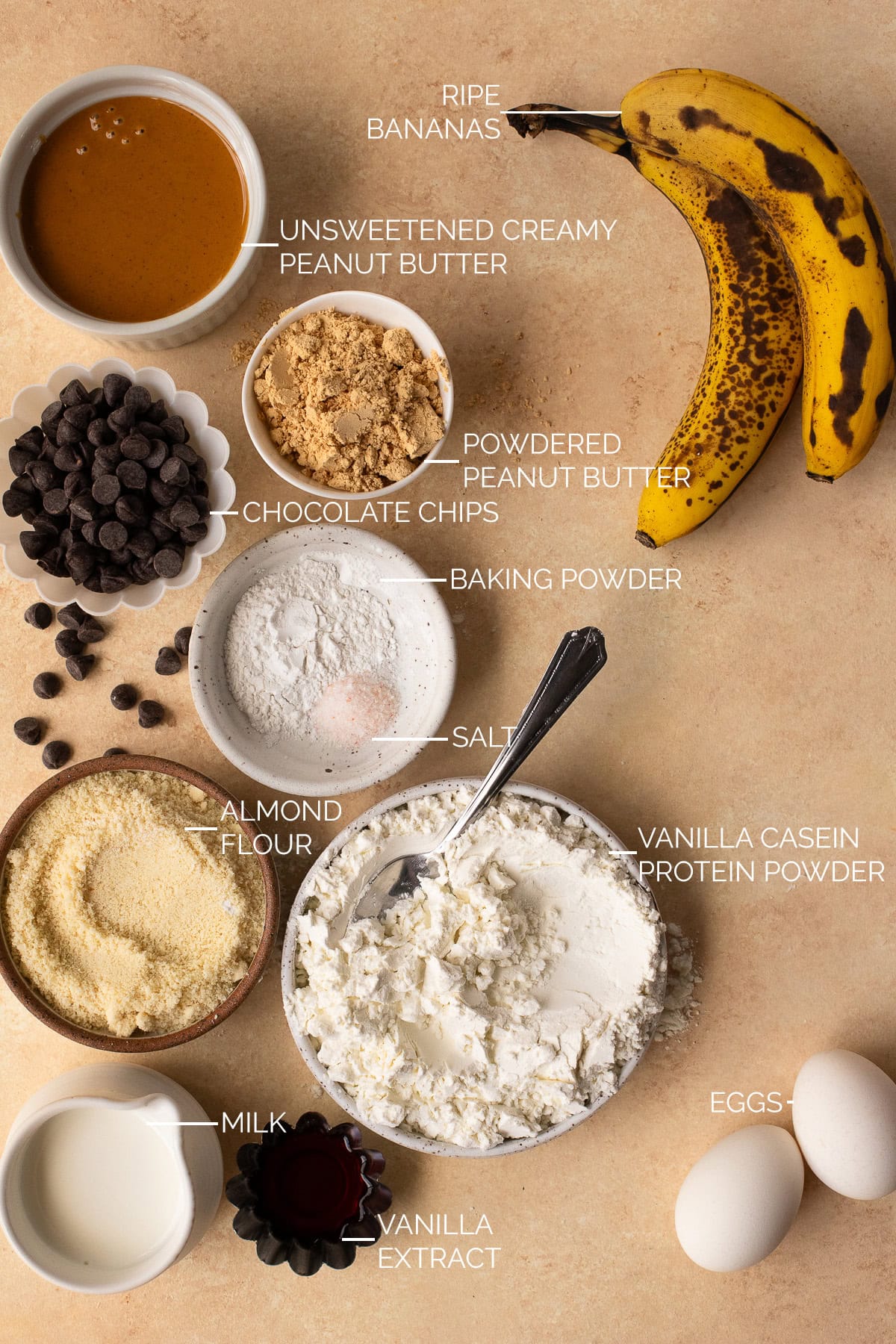 Ingredients portioned into bowls for banana protein muffins with protein powder, peanut butter, and chocolate chips.
